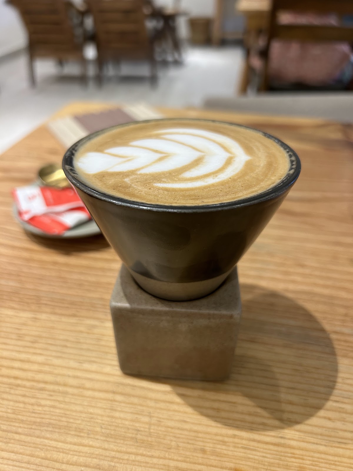 A latte with leaf art in a black ceramic cup, raised on a small stone pedestal.