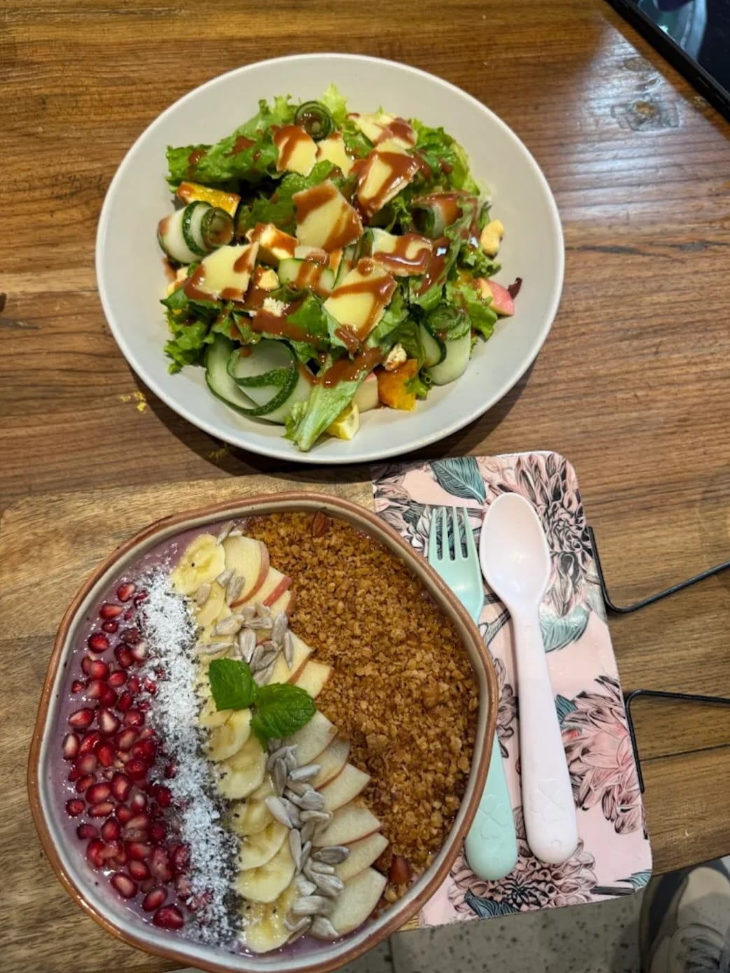 A garden salad and a healthy yogurt bowl with pomegranate, banana, granola and apple.
