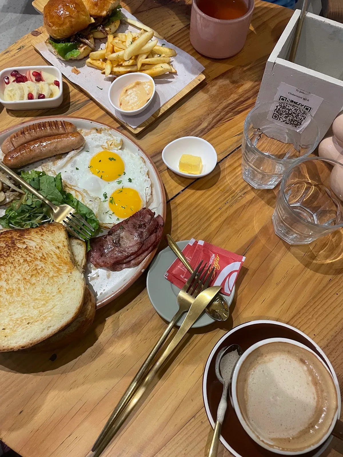 The signature CinderMint brunch platter — fried eggs, sausages, bacon, salad, fries and golden toast on a wooden table.